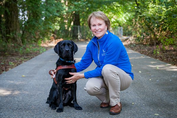 Christine Benninger kneels next to a black Lab guide dog