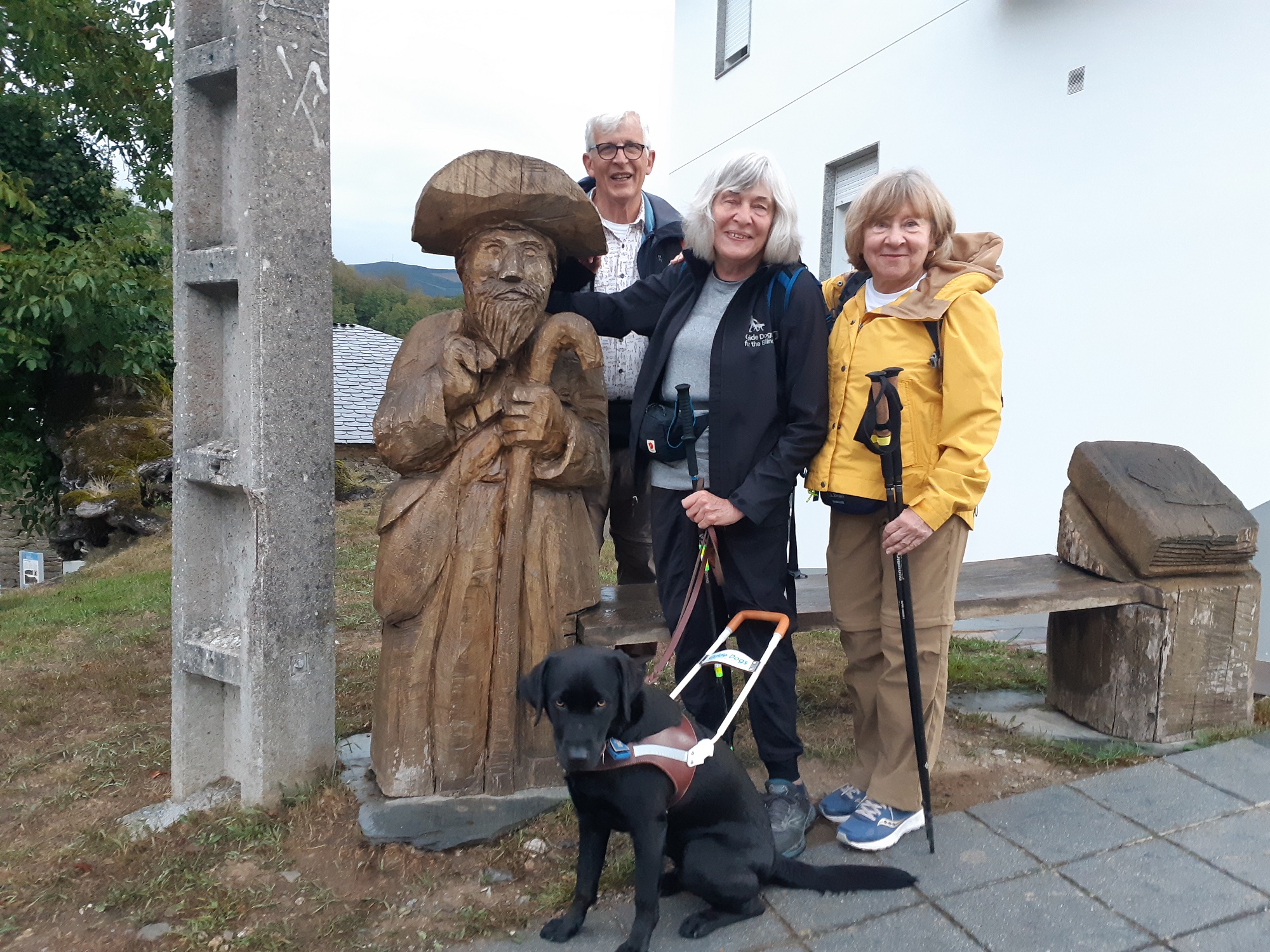 Joan with her black Lab guide dog and two friends Deb and John stand next to a wooden statueof St. James along the Camino.